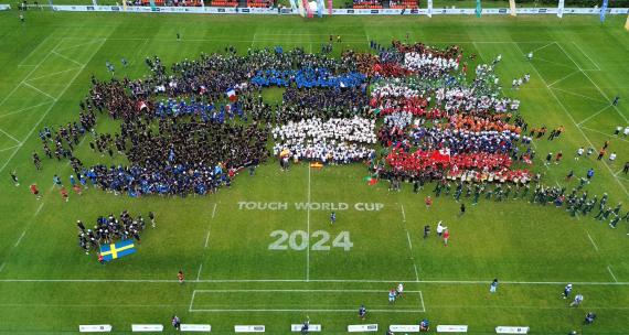 Overhead shot of the rugby pitch with teems assembled and showing the 2024 Touch world Cup logo stencilled on the grass