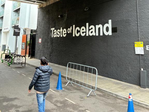 Large Taste of Iceland wall mural - white text on black bricks with person walking past