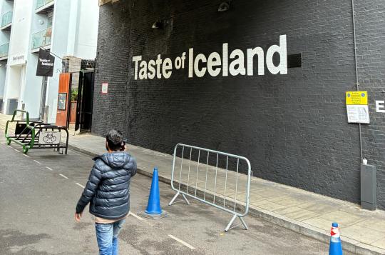 Large Taste of Iceland wall mural - white text on black bricks with person walking past