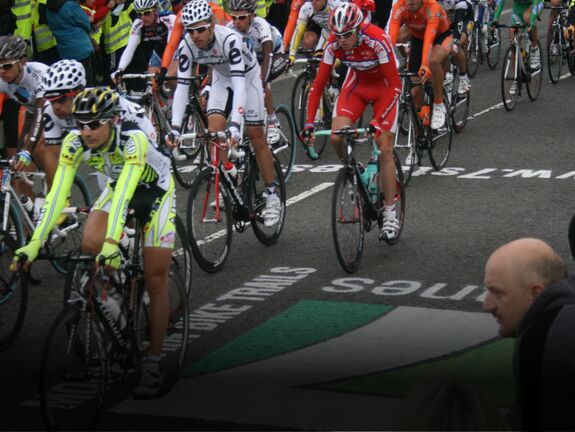 Road cyclists racing past the 7 Stanes logo applied to the road for the Tour of Britain event in Dumfries & Galloway