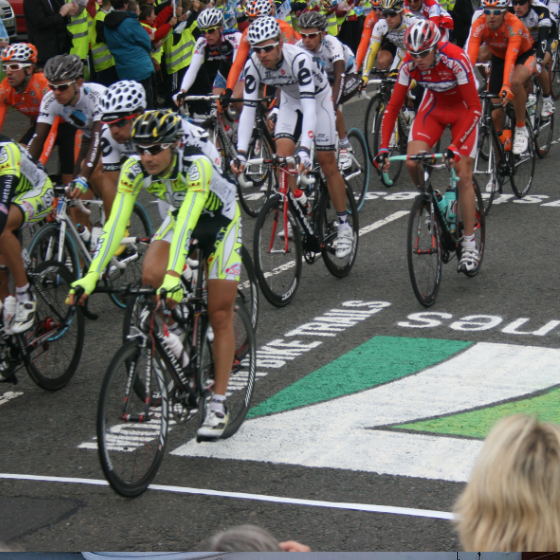 Road cyclists competing in the Tour of Britain crossing the 7 Stanes logo stencilled on the road