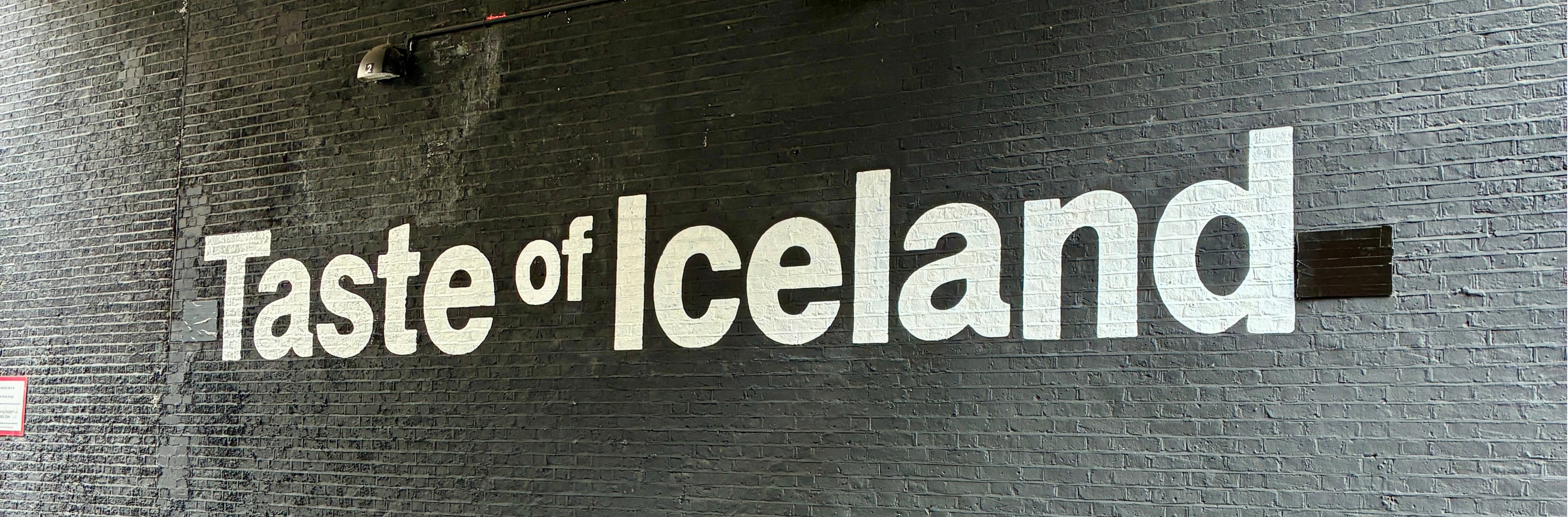 Large Taste of Iceland wall mural - white text on black bricks with person walking past